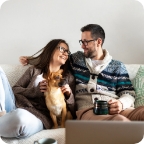 Couple sit on couch with a small dog on their laps.